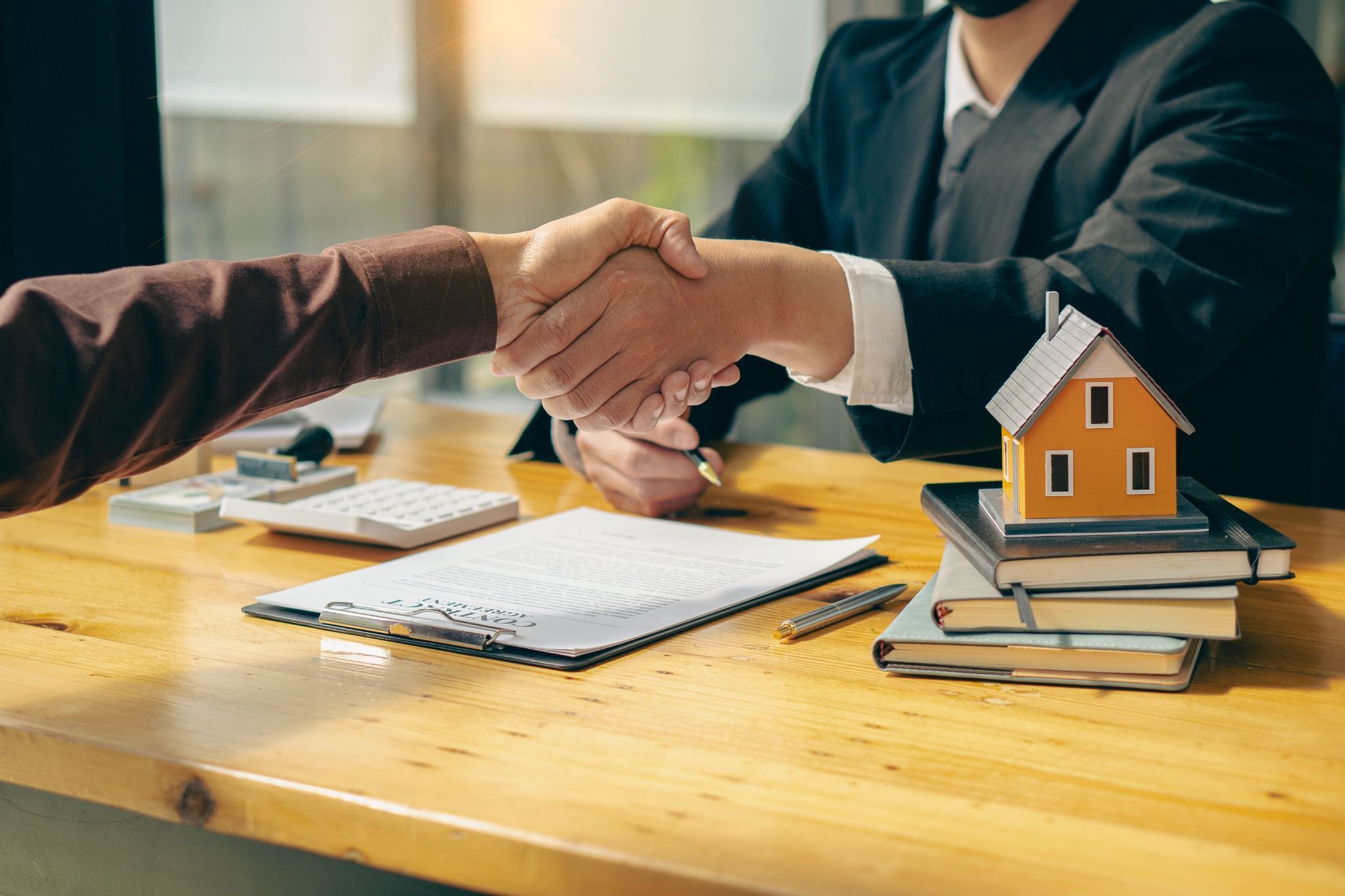 1. Two people shaking hands over a desk with a house model, symbolizing a successful home buying agreement.